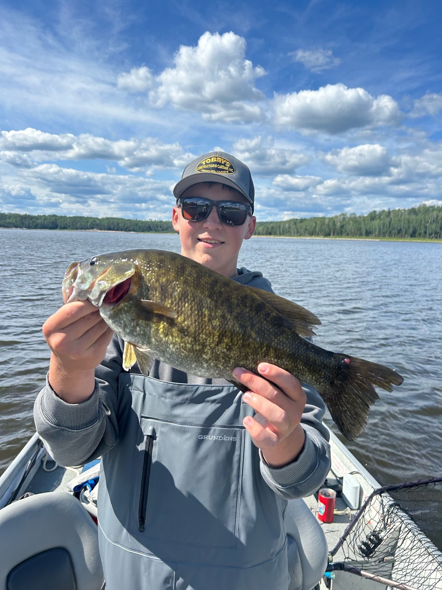 A man is holding a large smallmouth bass in his hands while on a boat.