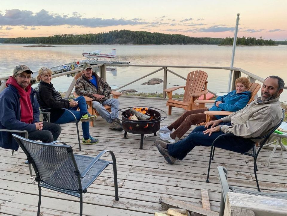 A group of people are sitting around a fire pit on a dock.