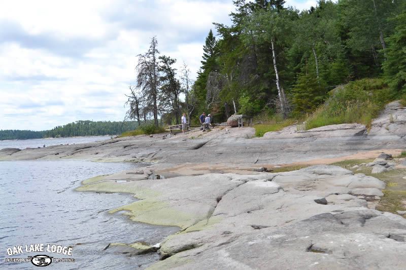 A group of people are walking on a rocky beach next to a lake.