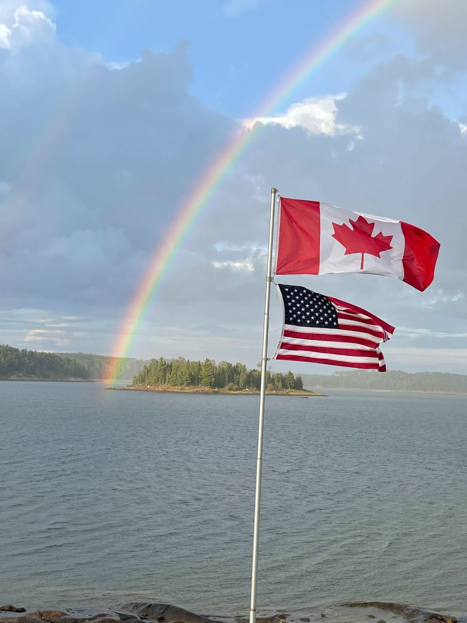A canadian flag and an american flag with a rainbow in the background