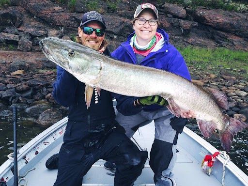 A man and a woman are holding a large muskie in a boat.