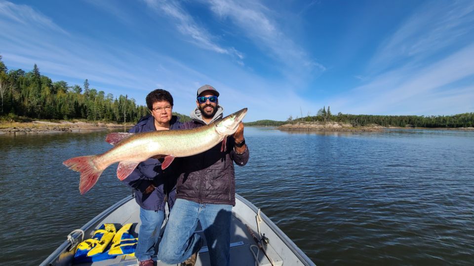 Two men are standing in a boat holding a large muskie at Oak Lake Lodge.