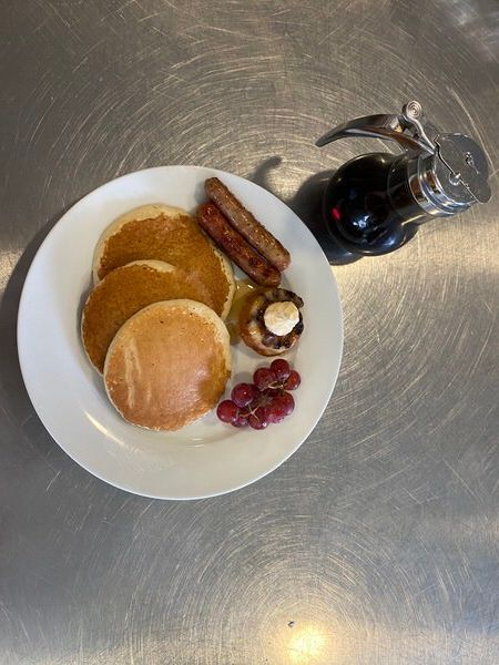 A white plate topped with pancakes , sausage , syrup and berries.