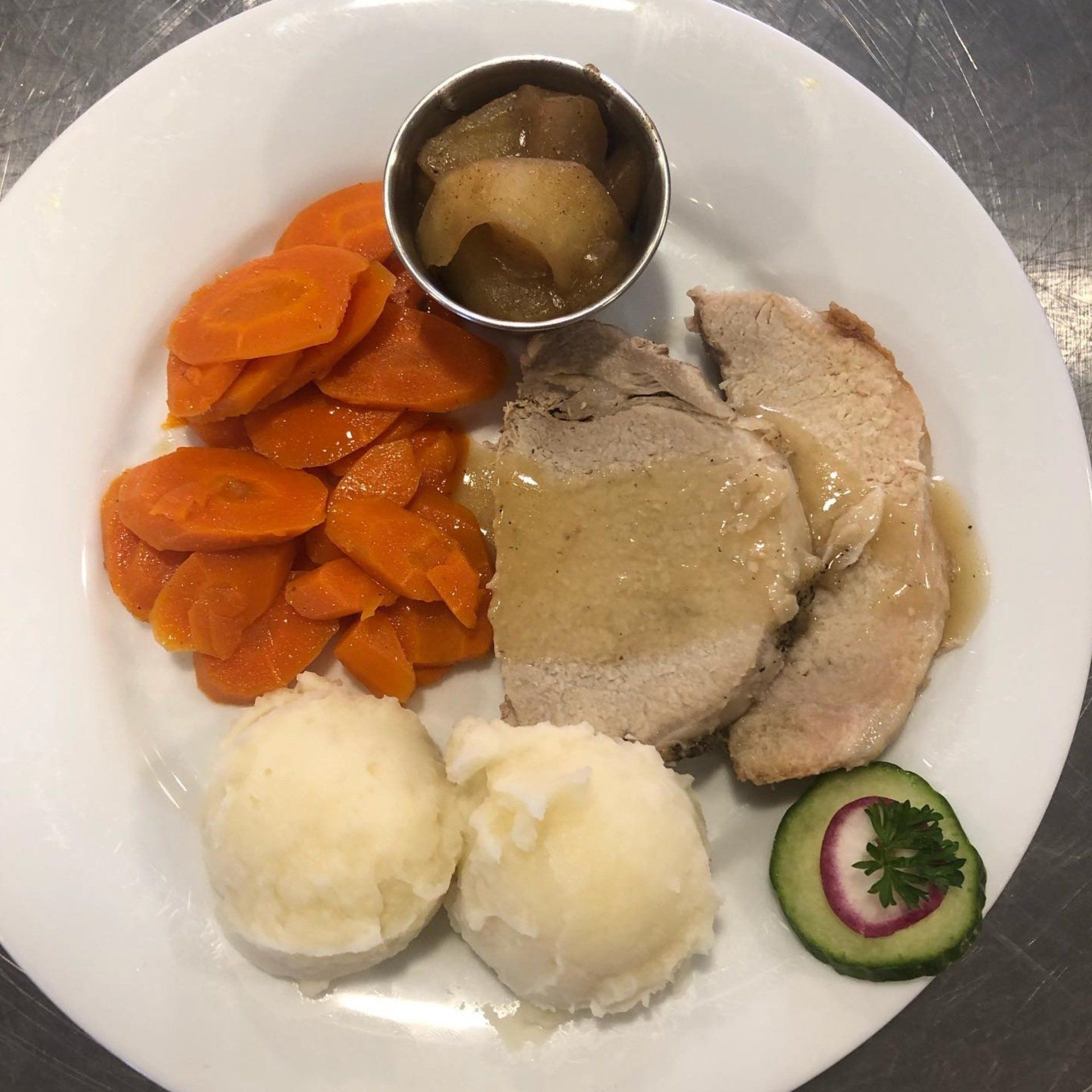 A white plate topped with meat , carrots , mashed potatoes and cucumbers.