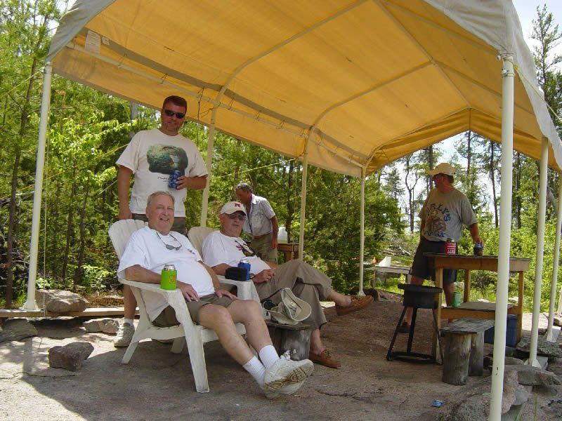 A group of men are sitting under a tent in the woods