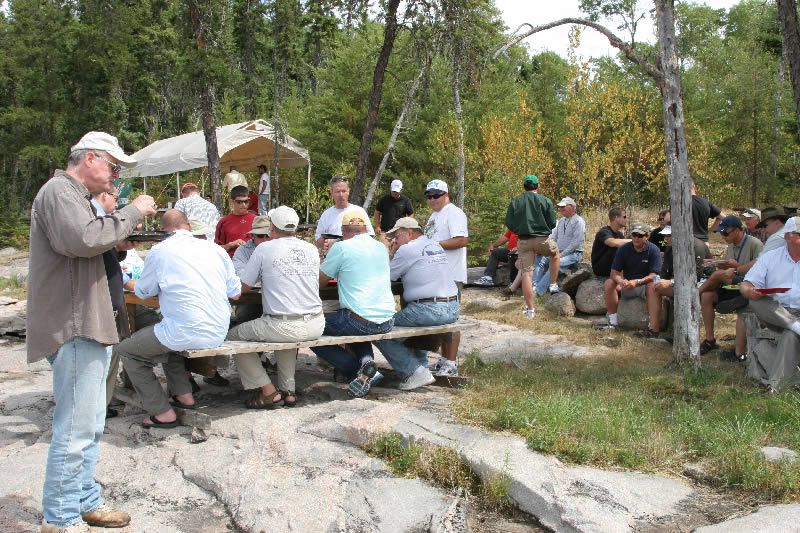 A group of men are sitting at a picnic table in the woods