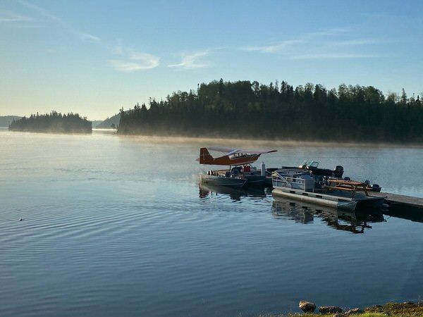 A small boat and a pontoon are docked at a dock on a lake.