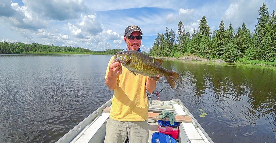 A man is holding a smallmouth bass  in a boat on a lake.