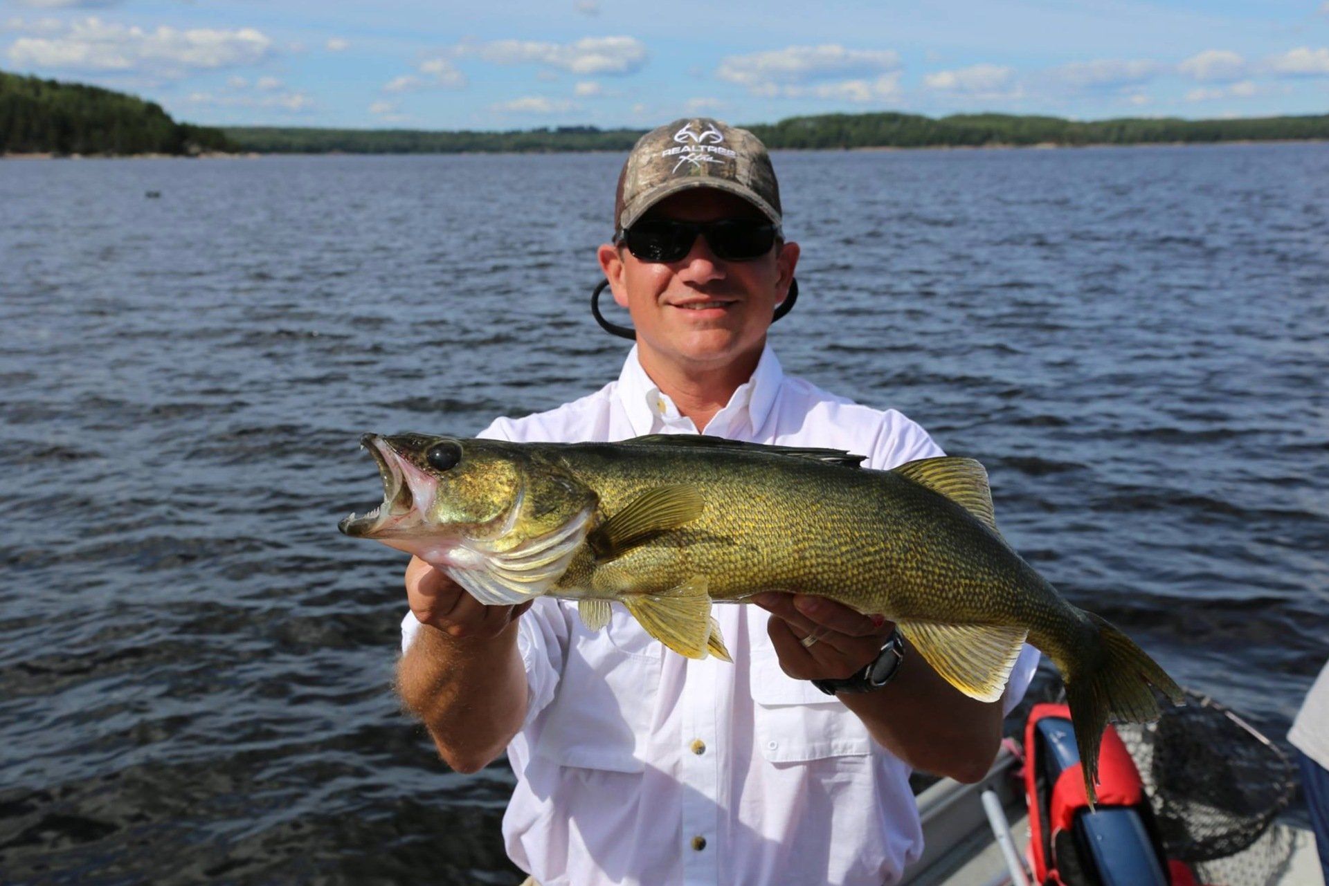 A man in a boat is holding a large walleye fish in his hands.