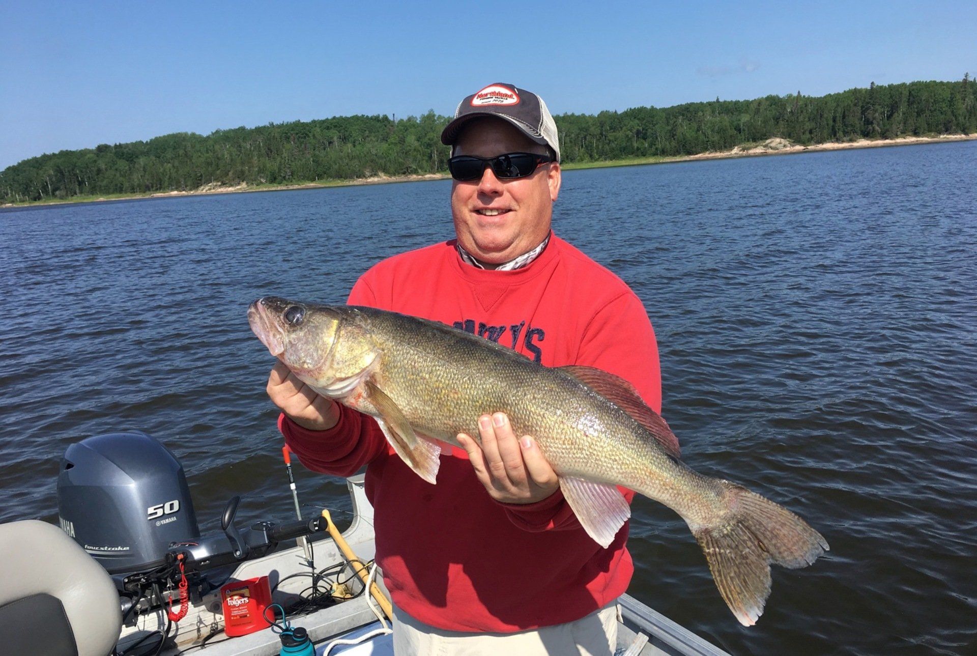 A man is holding a large walleye fish on a boat.