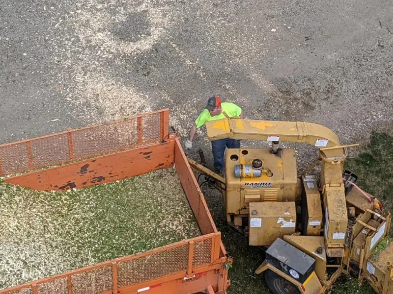 A man is loading wood chips into an orange trailer