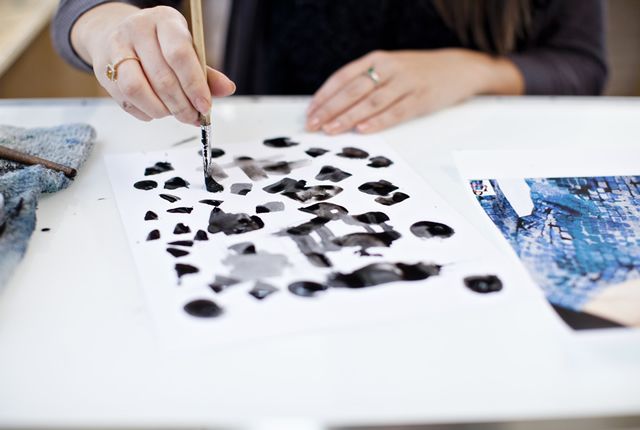 a woman is painting with a brush on a piece of paper .
