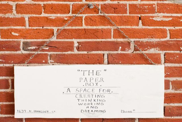 A sign on a brick wall that says The Paper Box