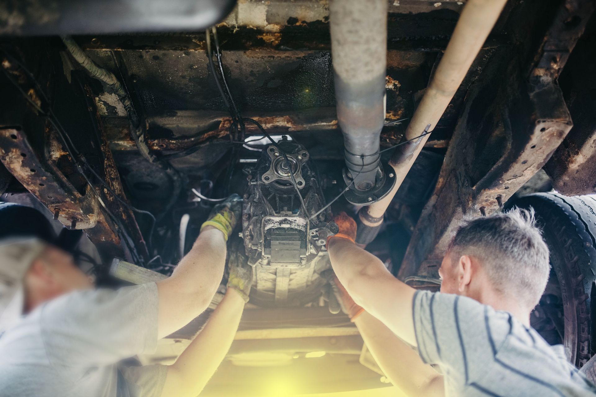 Two people working on the underside of a vehicle. They are using tools on the engine or transmission. Two people working on the underside of a vehicle. They are using tools on the engine or transmission.