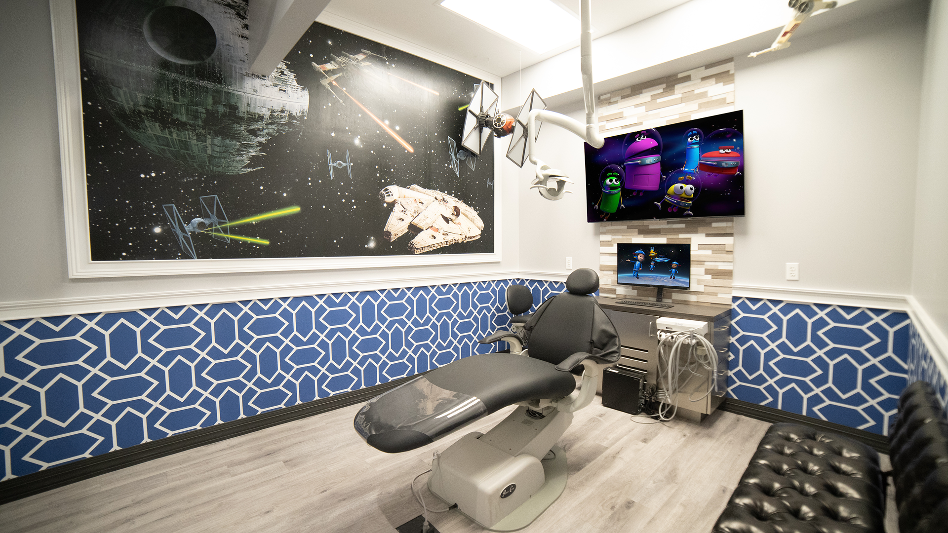 Modern dental exam room with chair, monitors, and blue geometric wall panels