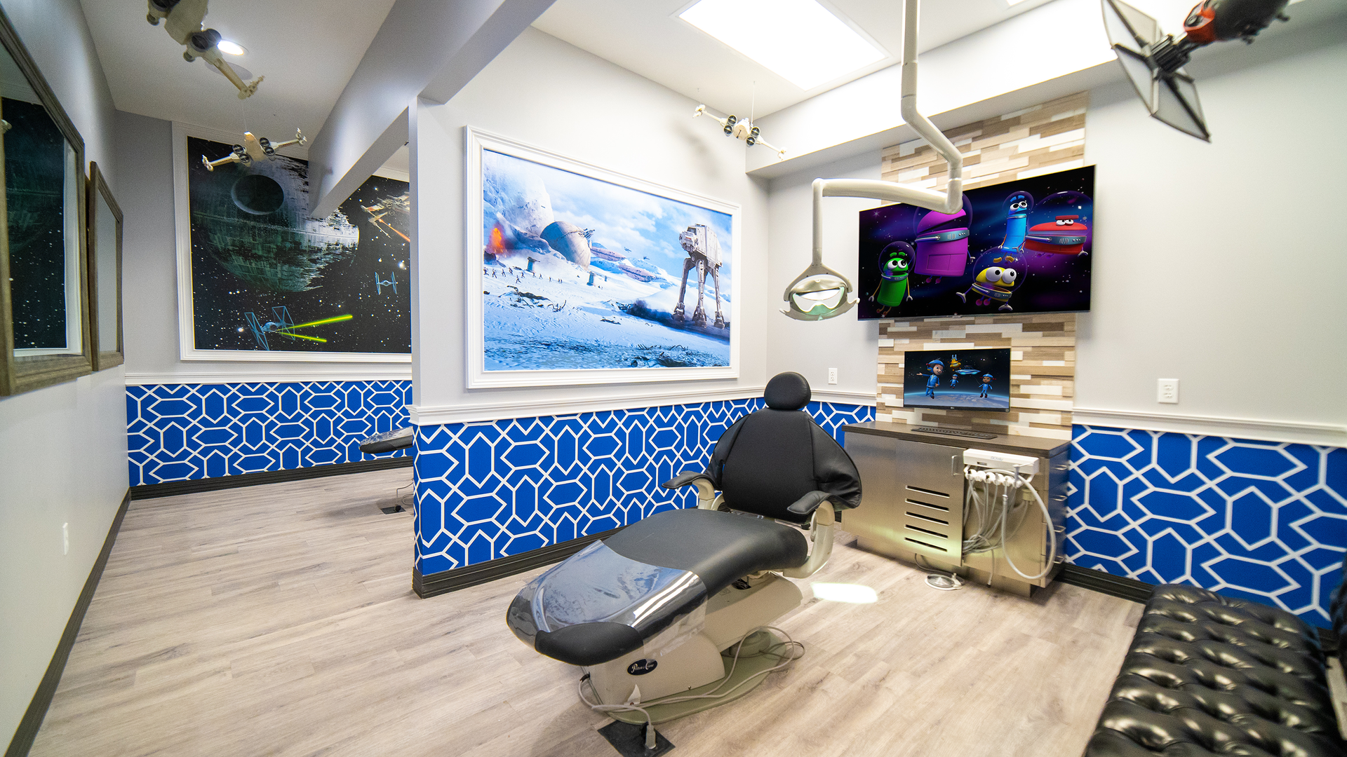 Modern treatment room with dental chair, wall-mounted screens, and blue wave-pattern decor