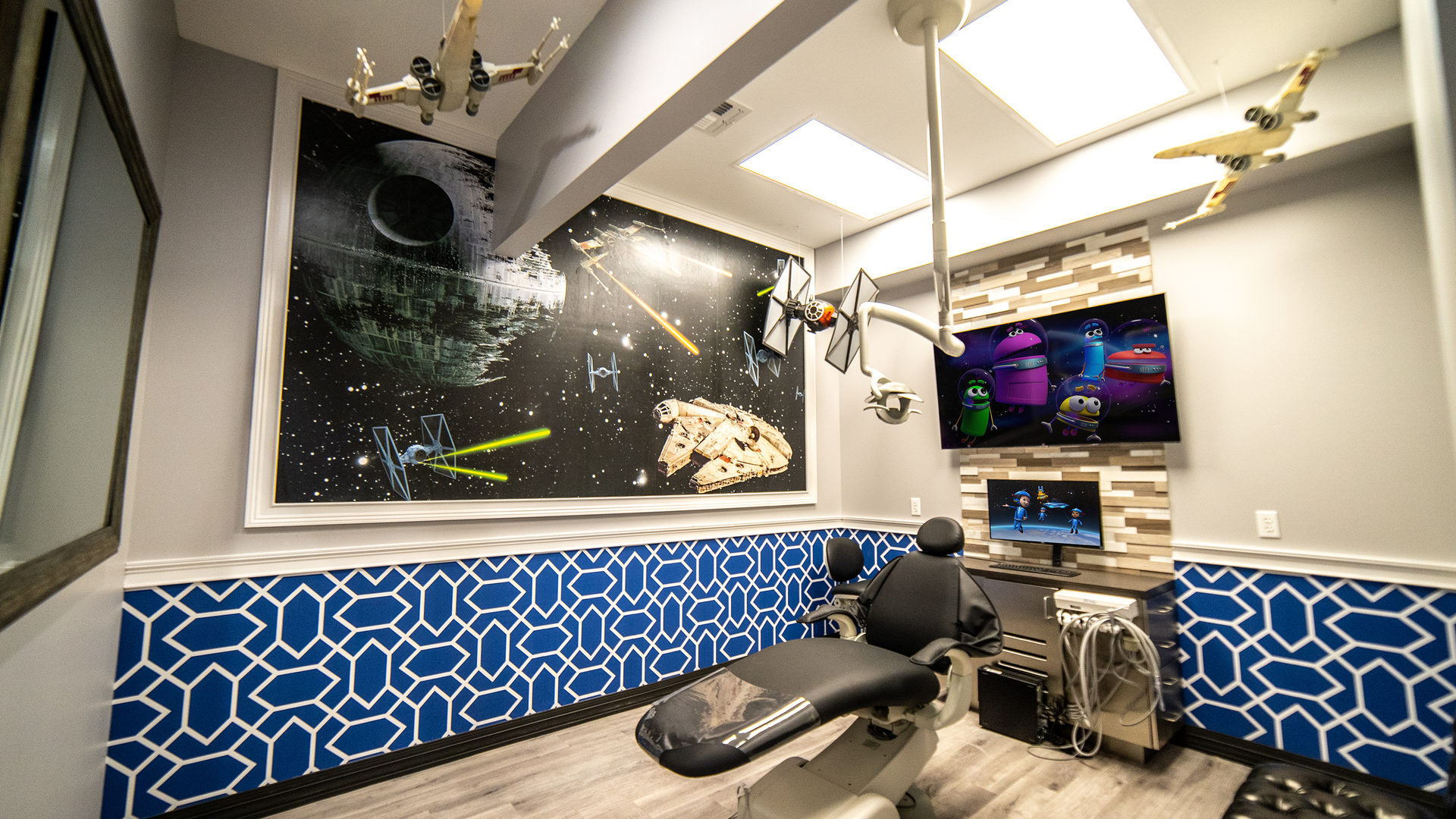 Modern space-themed lounge with blue patterned walls, black seating, and a wall-mounted TV