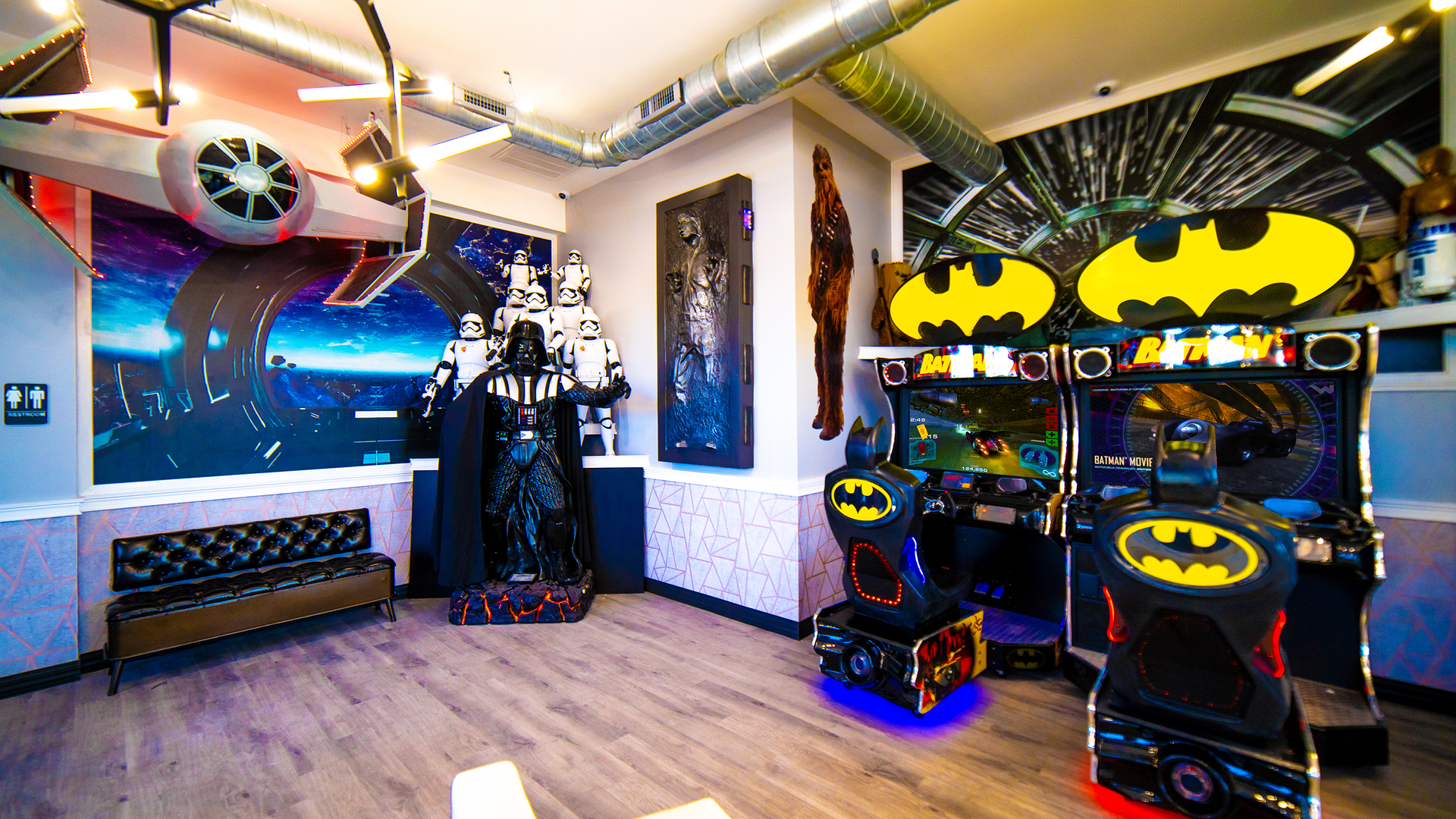 Batman-themed arcade room with two game cabinets, neon wall art, and a window seat