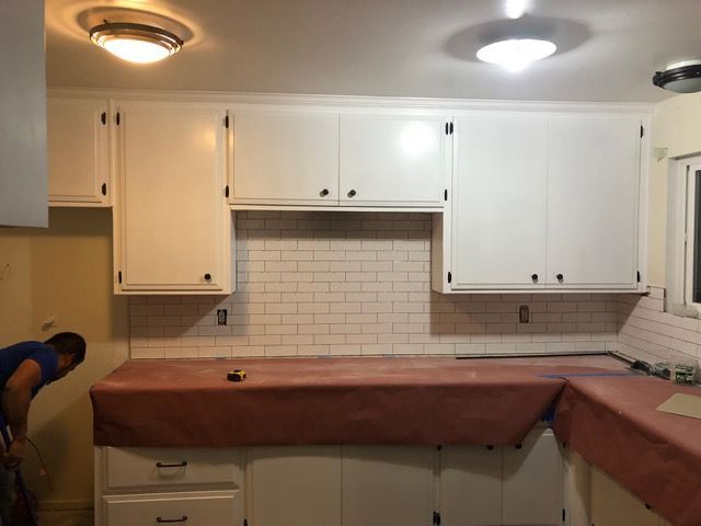 Kitchen renovation with white cabinets and tiled backsplash; countertops are covered with protective brown paper.