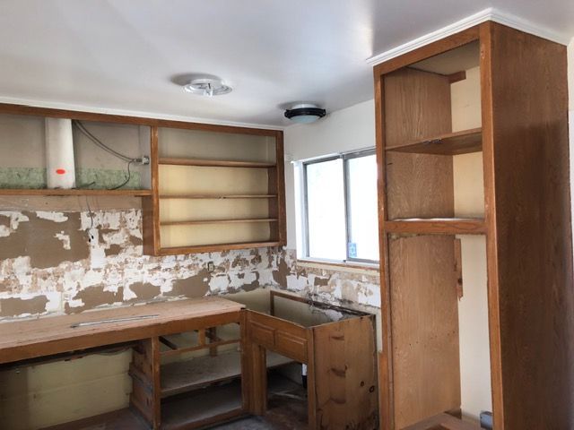 Small unfinished kitchen with wooden cabinets, sink, window, and exposed drywall walls