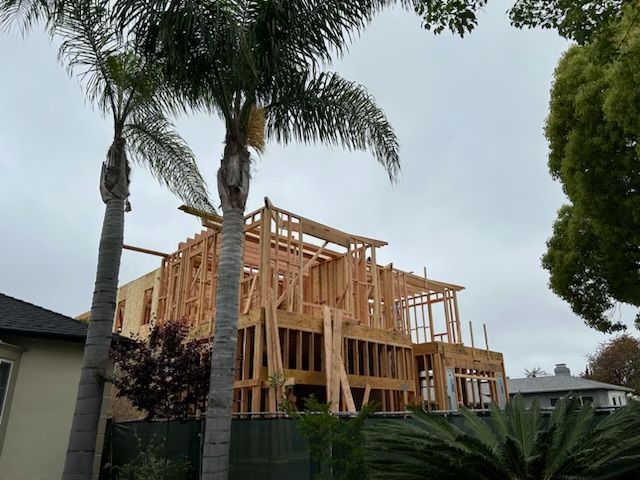 Wood-framed house under construction beside palm trees in a suburban neighborhood