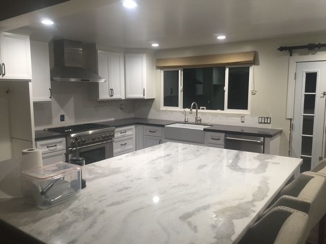 Modern kitchen with white cabinets, gray countertops, and a marble island under recessed lights
