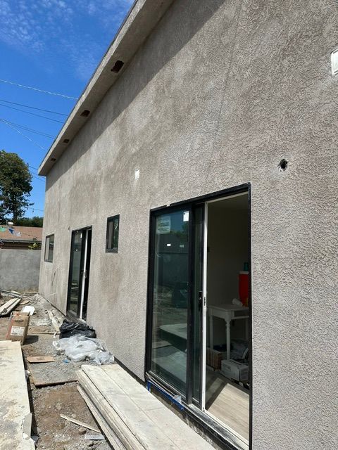 Exterior of a stucco house under construction with sliding glass doors and scattered строитель materials nearby