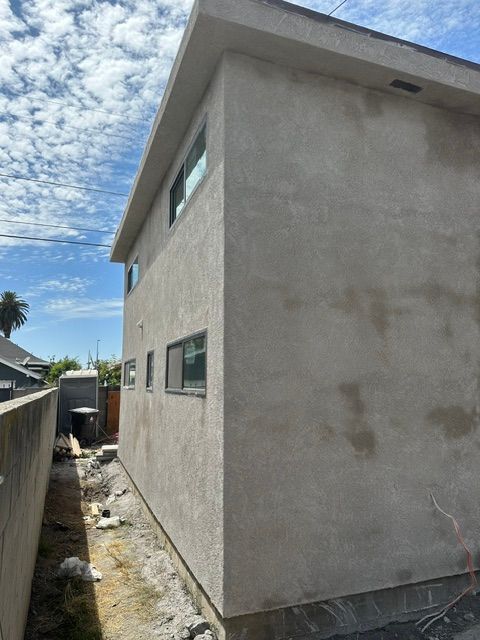Narrow side yard beside a gray stucco two-story house under a cloudy blue sky