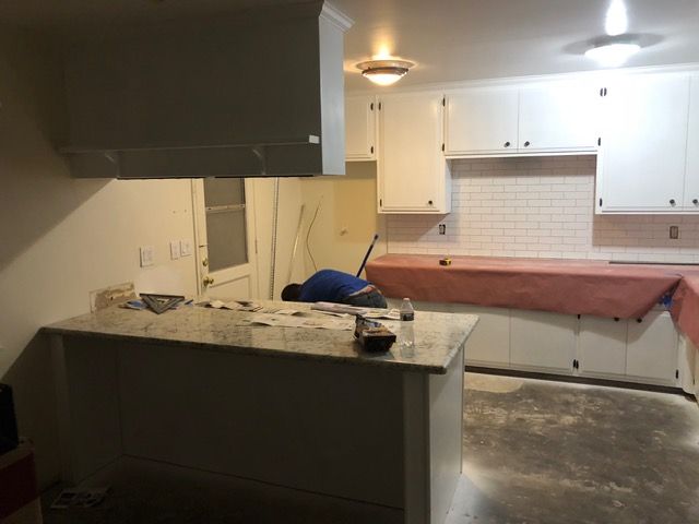 Kitchen under renovation with granite island, white cabinets, and covered countertops.