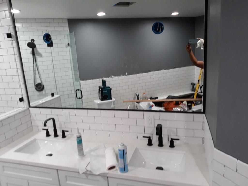 Modern bathroom with double sink, black fixtures, tiled shower, and a large mirror reflecting the room.