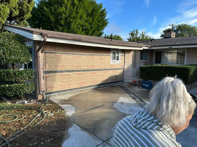 Driveway and brick garage beside a house, with wet concrete and a person in the foreground.