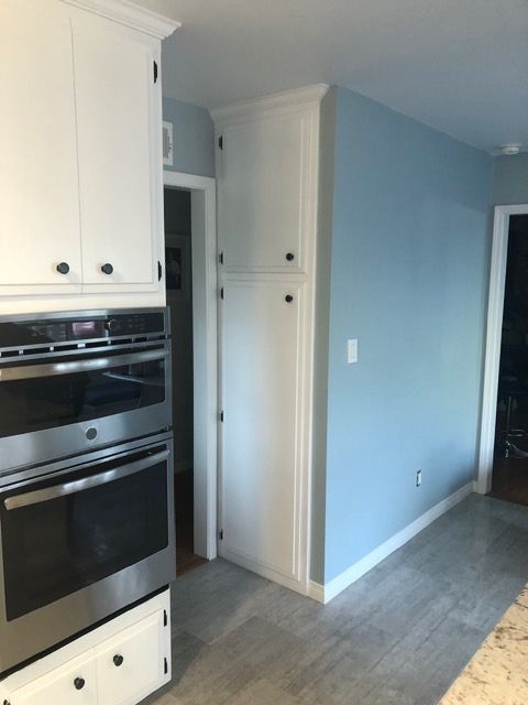 Kitchen hallway with white cabinets, built-in oven, and light blue walls leading to another room