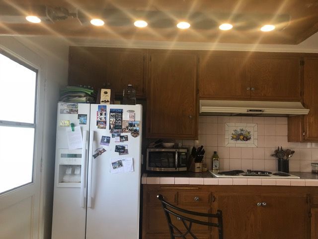 Small kitchen with wooden cabinets, white refrigerator, sink, stove, and a window letting in daylight.