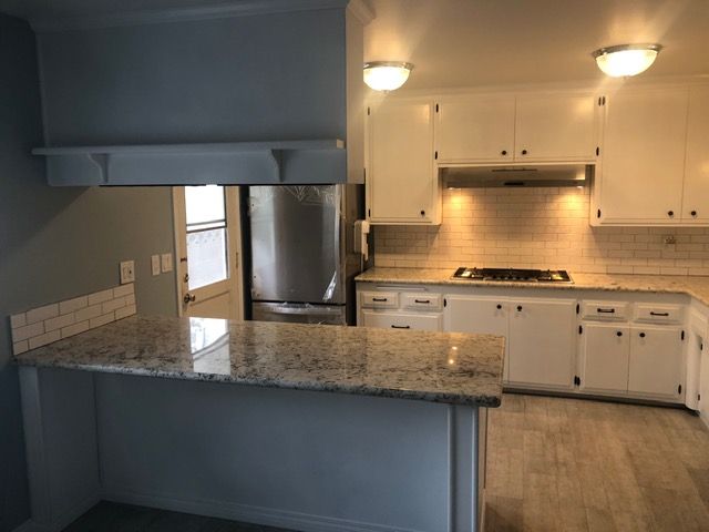 Modern kitchen with granite island, white cabinets, stainless appliances, and tiled backsplash