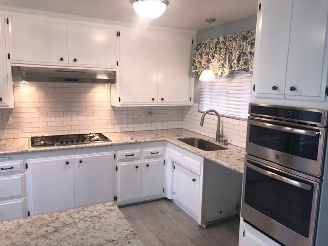 Bright white kitchen with granite counters, tiled backsplash, gas stove, sink, and double wall oven