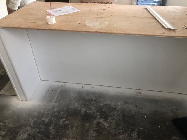 Dusty workbench in a bare room, with a white wall and dark stained floor.