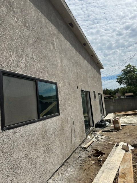 Exterior of a stucco house under construction with windows, doors, and lumber along the side wall
