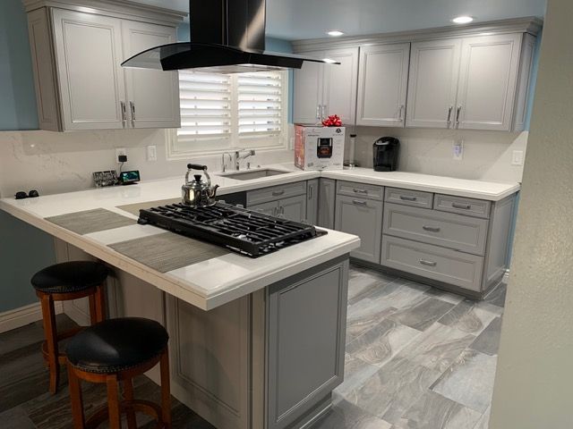 Modern gray-and-white kitchen with an island, black range hood, and two stools by the counter.