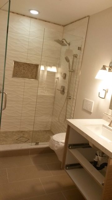 Modern bathroom with glass shower, beige tile, and vanity sink.