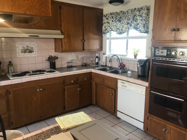 Compact kitchen with wood cabinets, tan countertops, white dishwasher, and a window above the sink