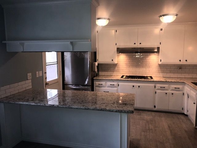 Modern kitchen with white cabinets, granite island, stainless steel appliances, and warm under-cabinet lighting