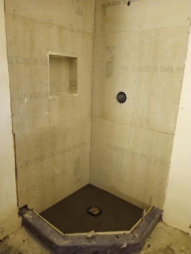 Small tiled shower stall with a built-in niche, wall-mounted fixture, and floor drain.