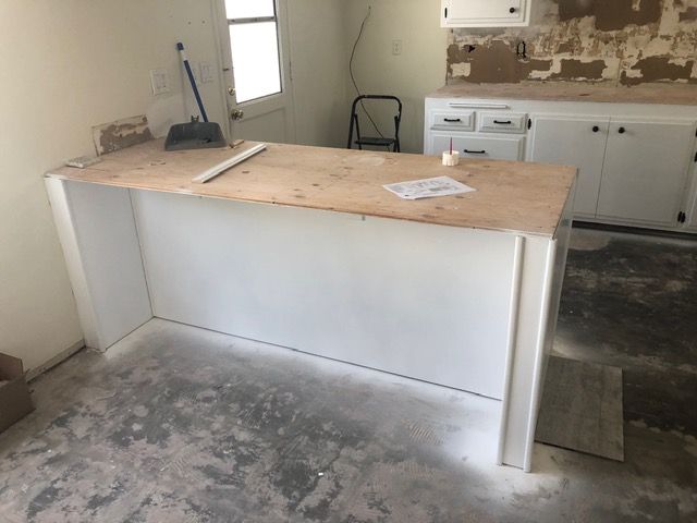 Partially renovated kitchen with a white island, unfinished floor, and tools on the countertop