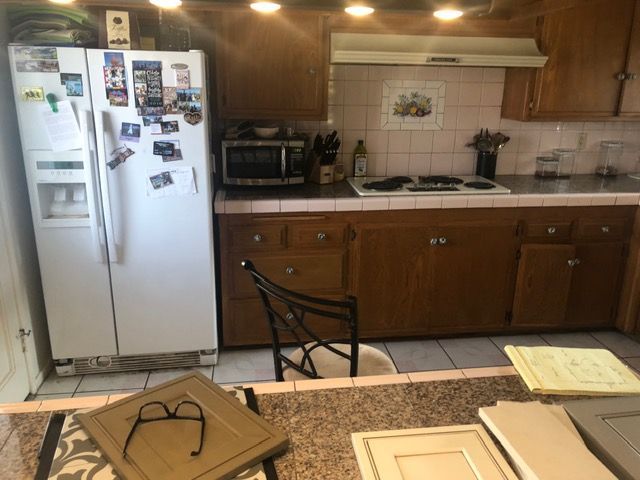 Small kitchen with white refrigerator, wooden cabinets, stove, microwave, and granite counter with papers.