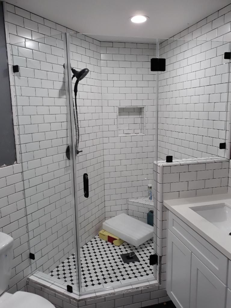 White tiled accessible shower with grab bars, fold-down bench, handheld shower, and black-and-white mosaic floor