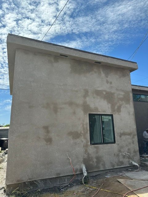 Small stucco house exterior with a window and exposed plumbing under a blue sky