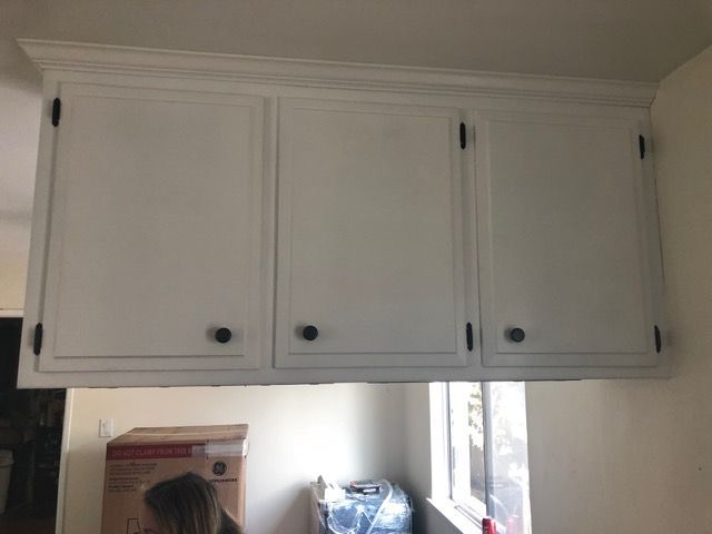 White kitchen wall cabinets above a counter with window light and boxes below