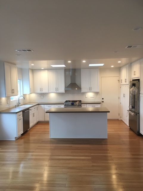 Bright modern kitchen with white cabinets, island, stainless appliances, and hardwood floors