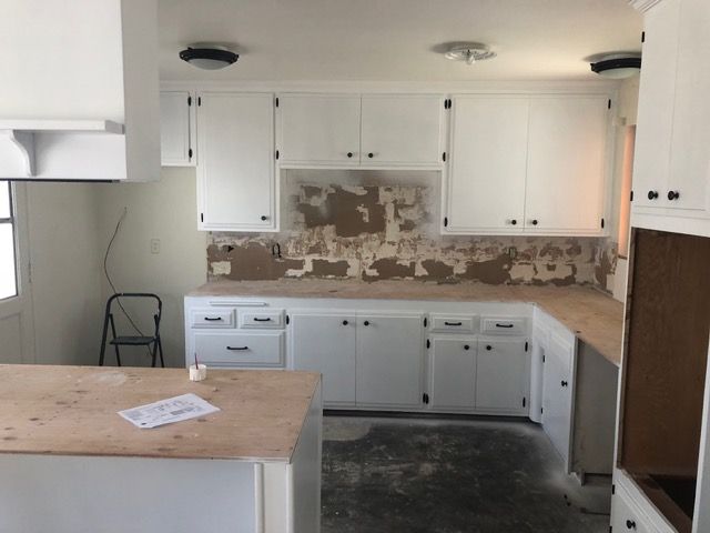 Kitchen under renovation with white cabinets, brown countertops, and exposed backsplash area
