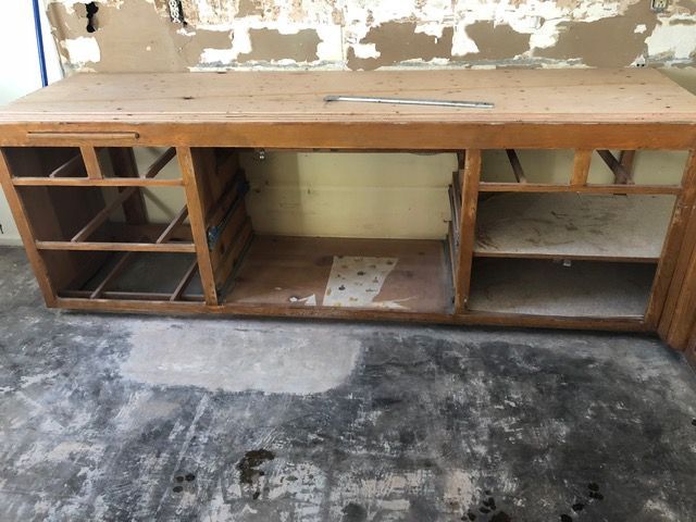 Worn wooden workbench with open shelves against a peeling wall in a bare room